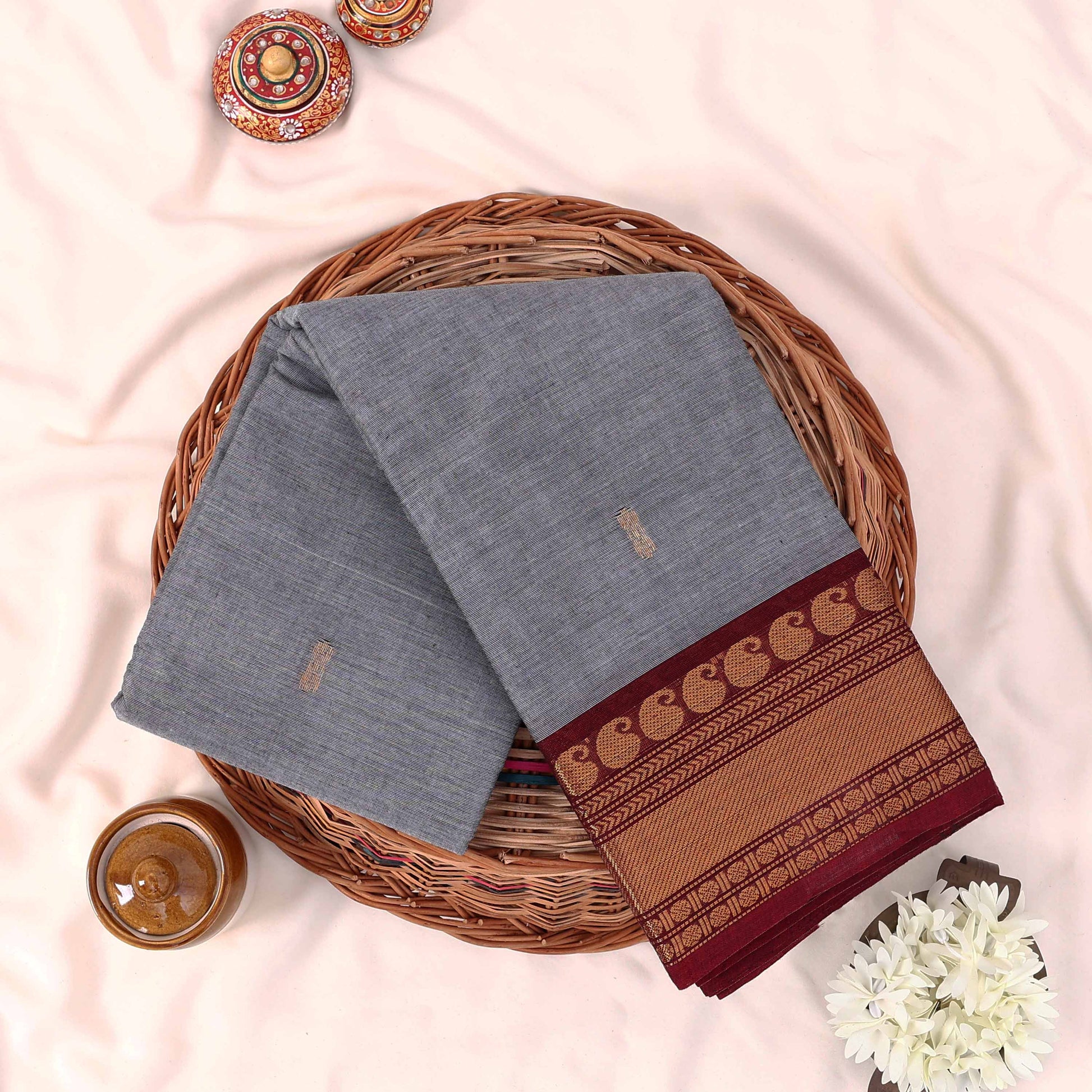 Kanchi Cotton Saree With Grey Body And Maroon Gold Zari Border Folded Flat Lay View In Wicker Basket
