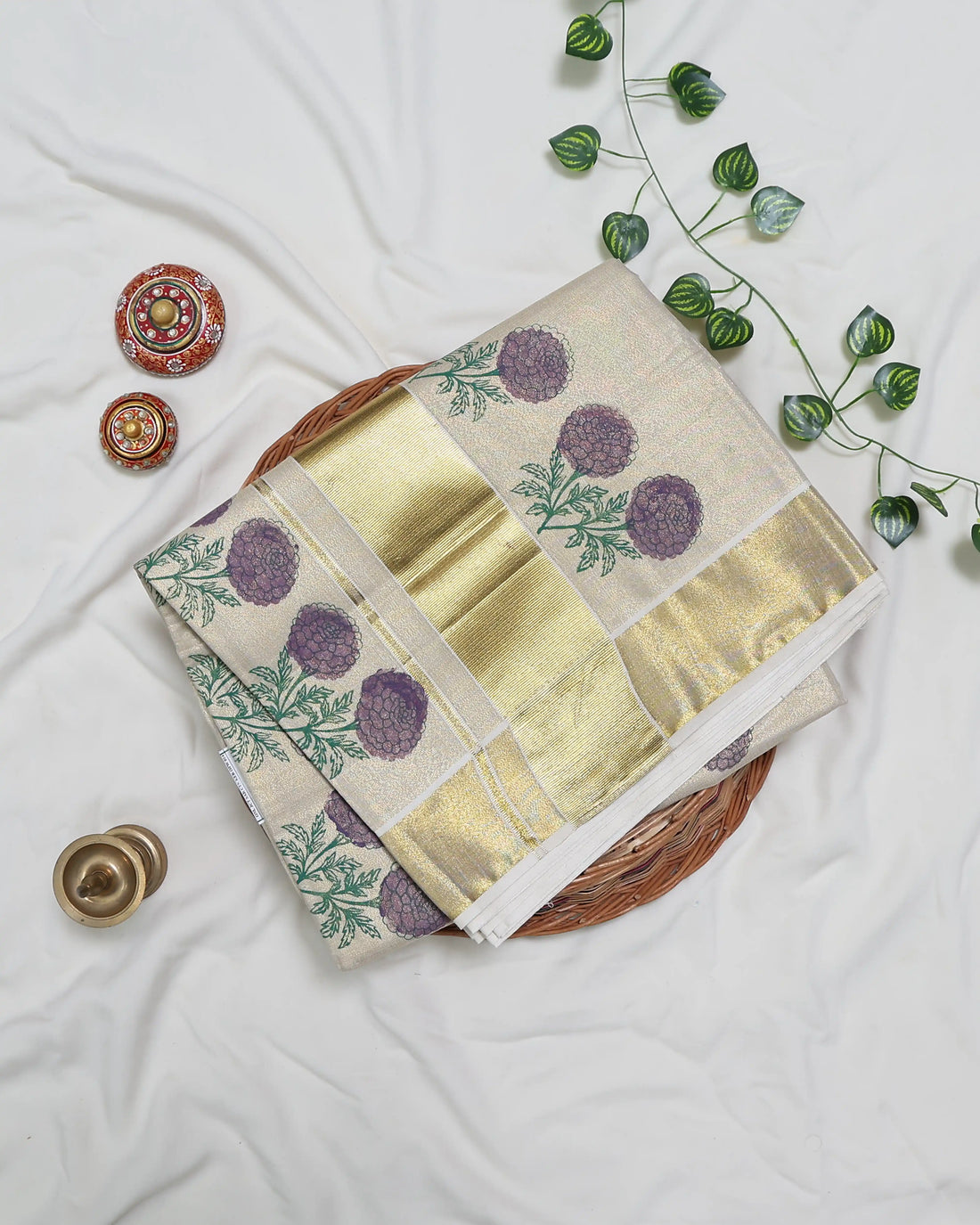 A cream-colored kerala saree with a metallic gold border and purple floral embroidery near the hem full view