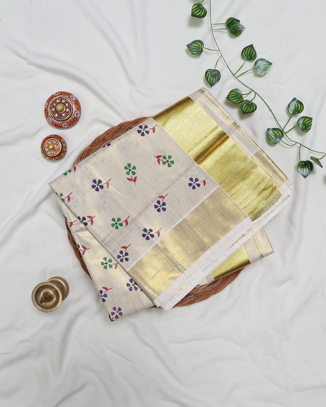 A cream-colored kerala saree with gold zari stripes and small colorful floral motifs, full view