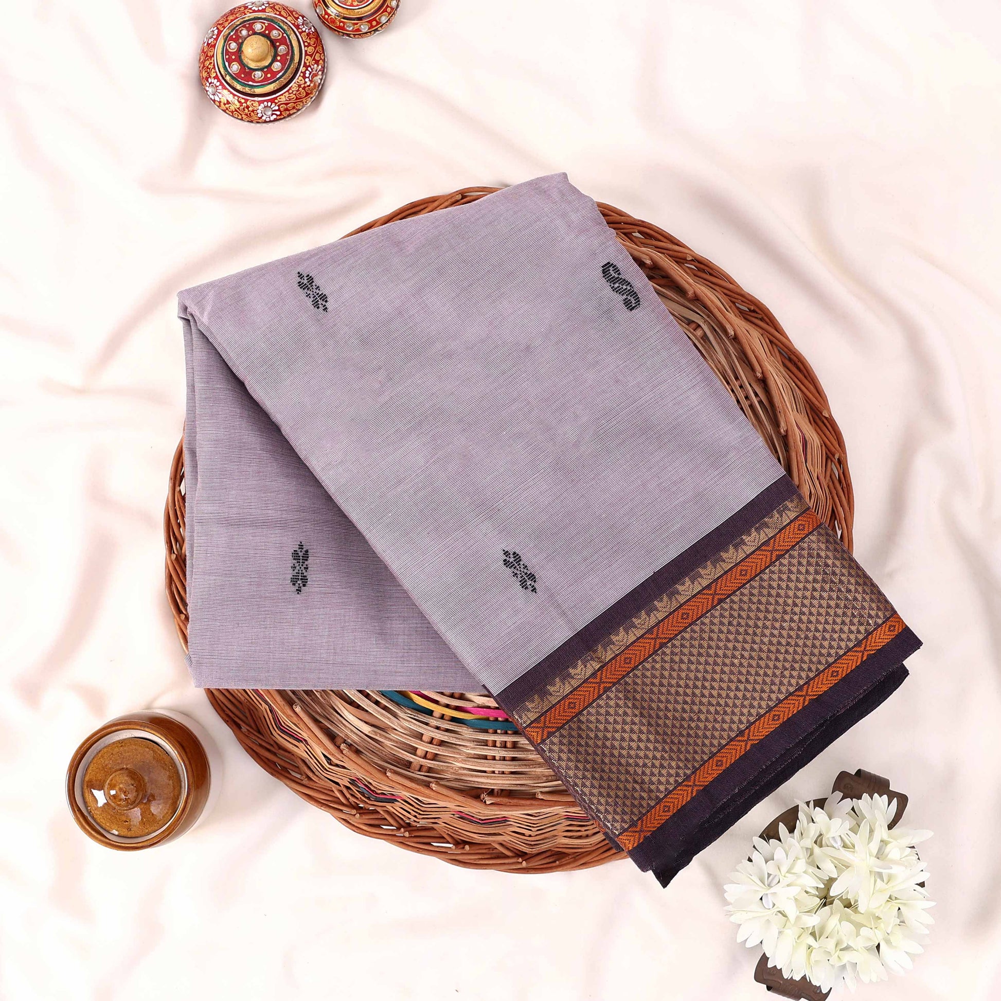 Kanchi Cotton Saree With Zari Border In Lavender Neatly Folded On Wicker Basket Top View Display
