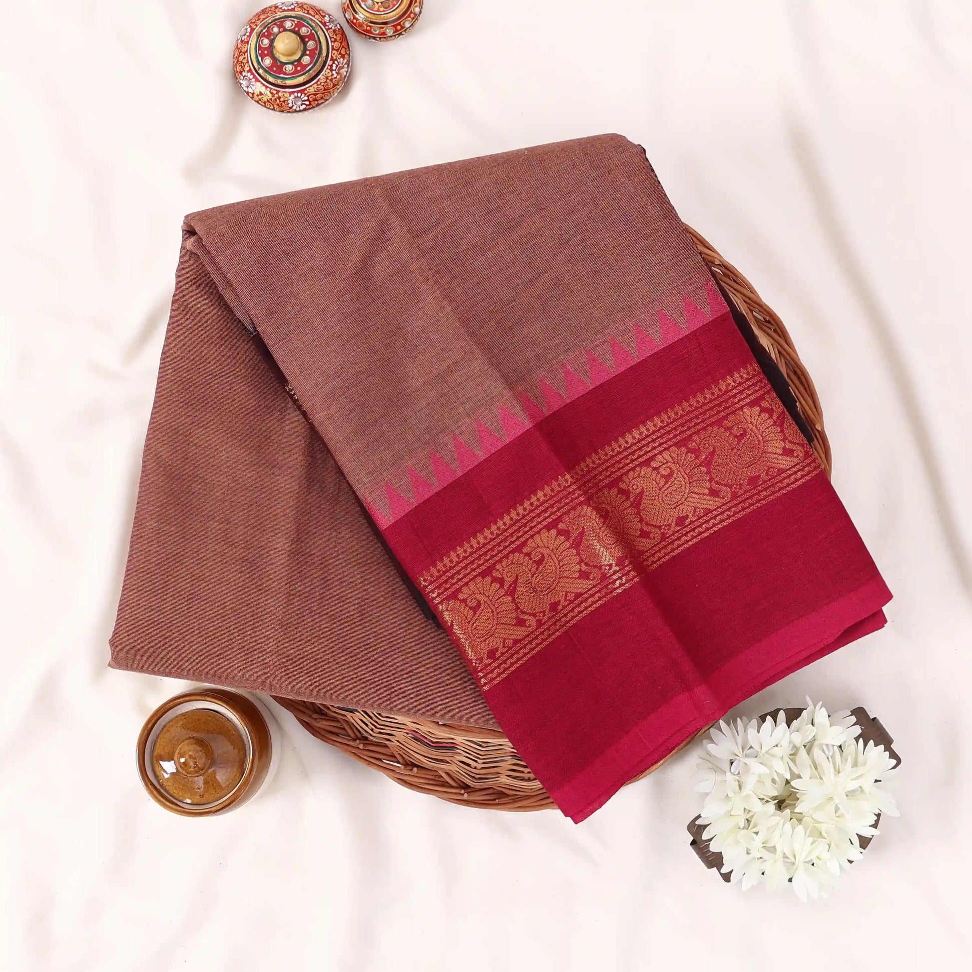 Chettinad cotton saree in brown with a contrast magenta zari woven peacock border folded flat lay front view.