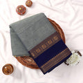 Kanchi Cotton Saree With Light Green Body And Navy Blue Zari Border Folded On Wicker Basket Top View
