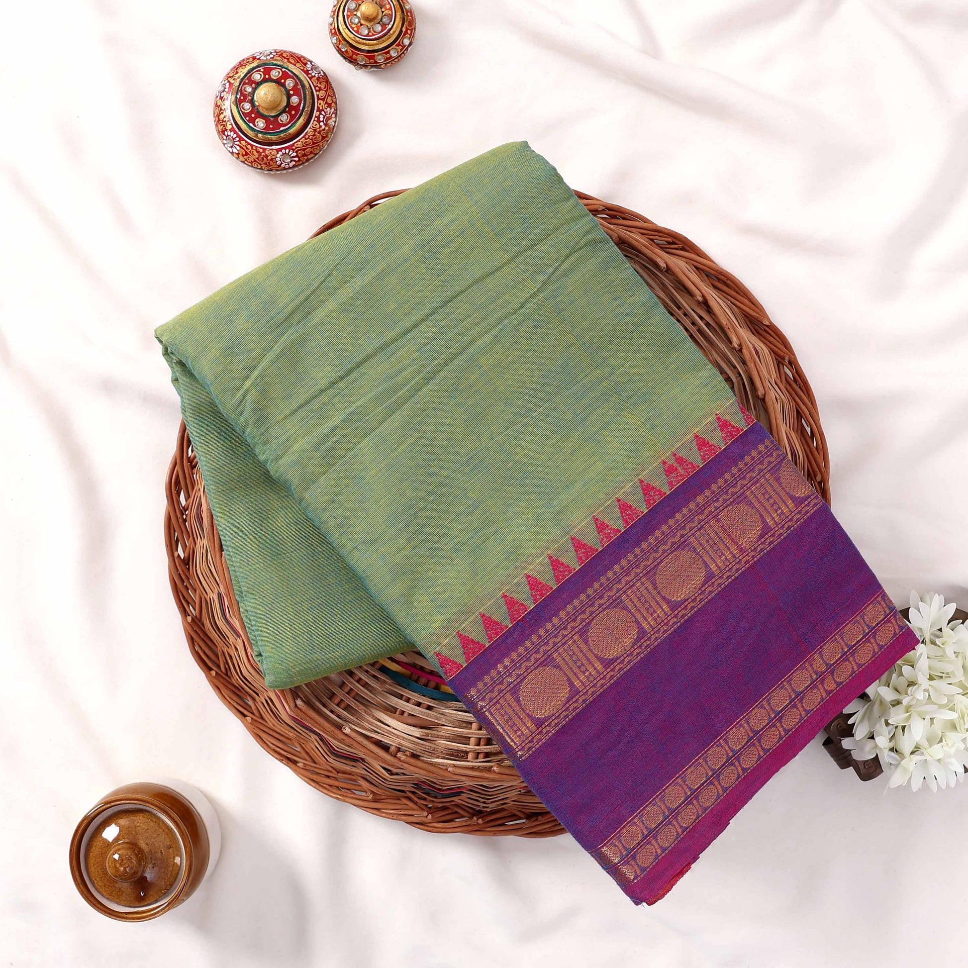 Kanchi Cotton Saree With Zari Woven Purple Border And Pastel Green Body Folded Flat Lay View With Decorative Accents
