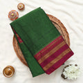 A folded dark green saree or fabric piece with a deep red border and gold woven stripes