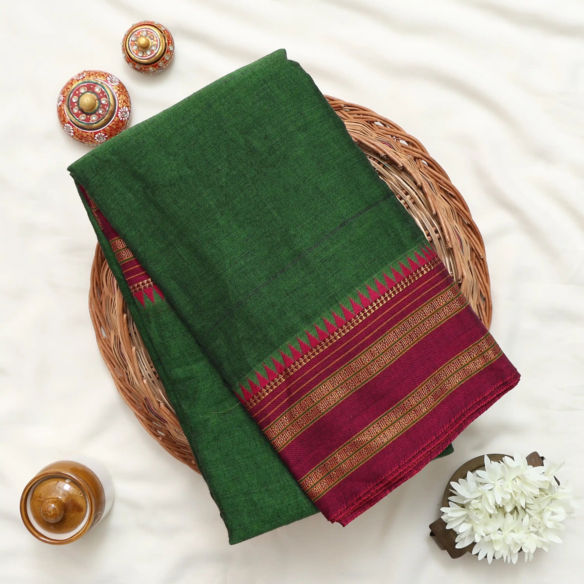 A folded dark green saree or fabric piece with a deep red border and gold woven stripes