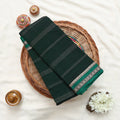 A folded dark green saree with white stripes and a patterned border