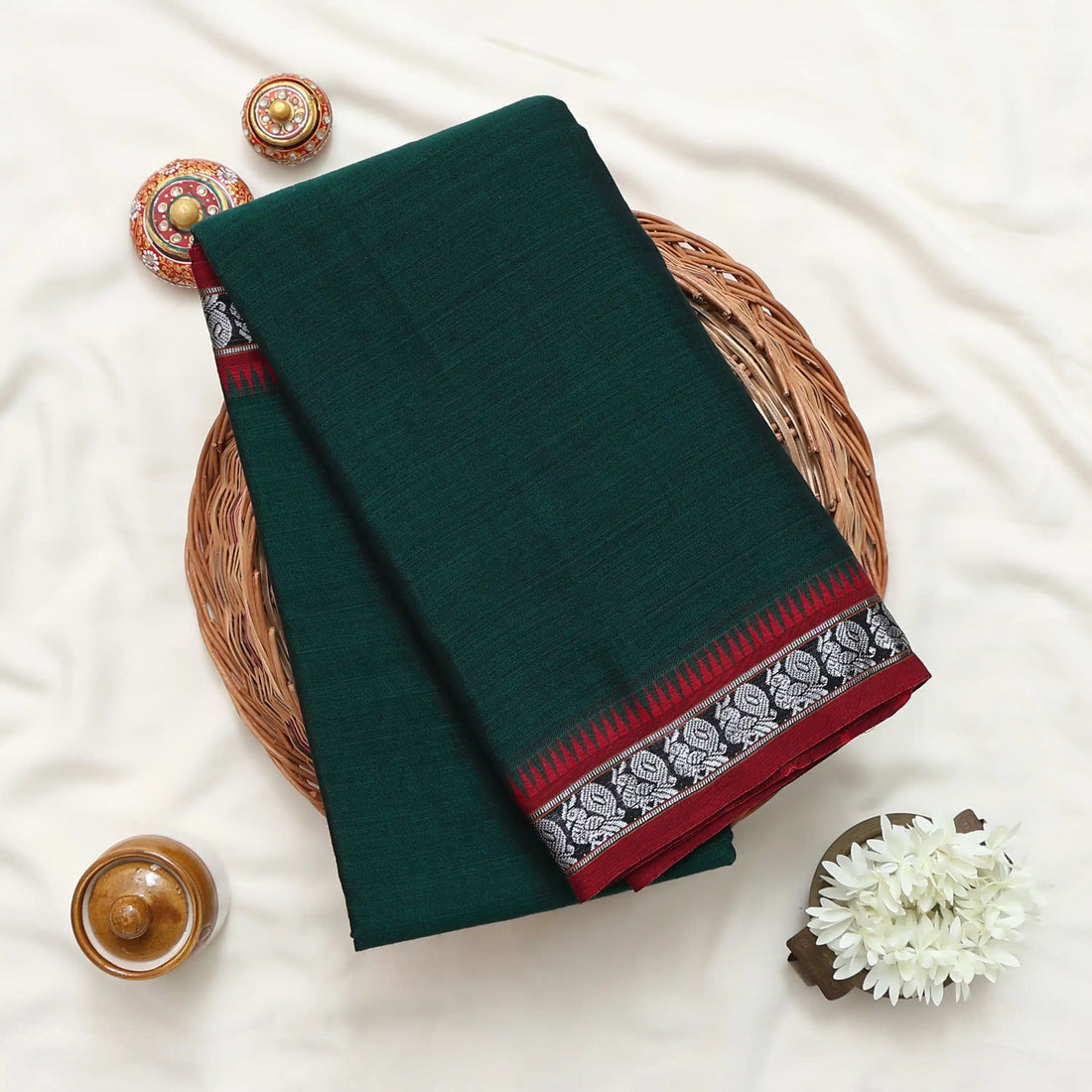 A dark green saree with red and silver patterned borders