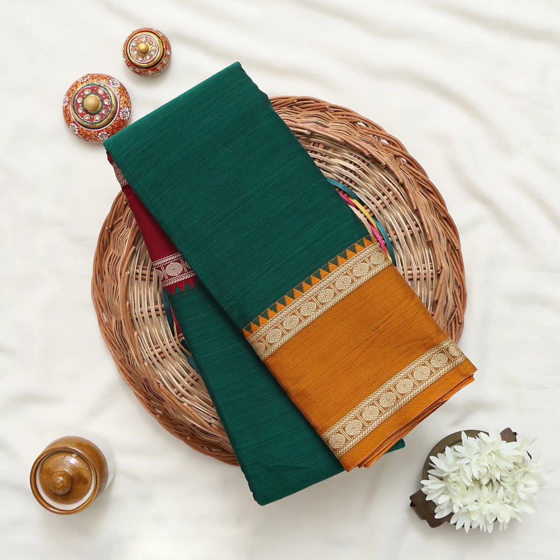 A dark green silk saree with a wide mustard yellow and gold checkered border, blouse is maroon with gold  woven borders.