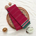 A folded deep red saree with green and white border details