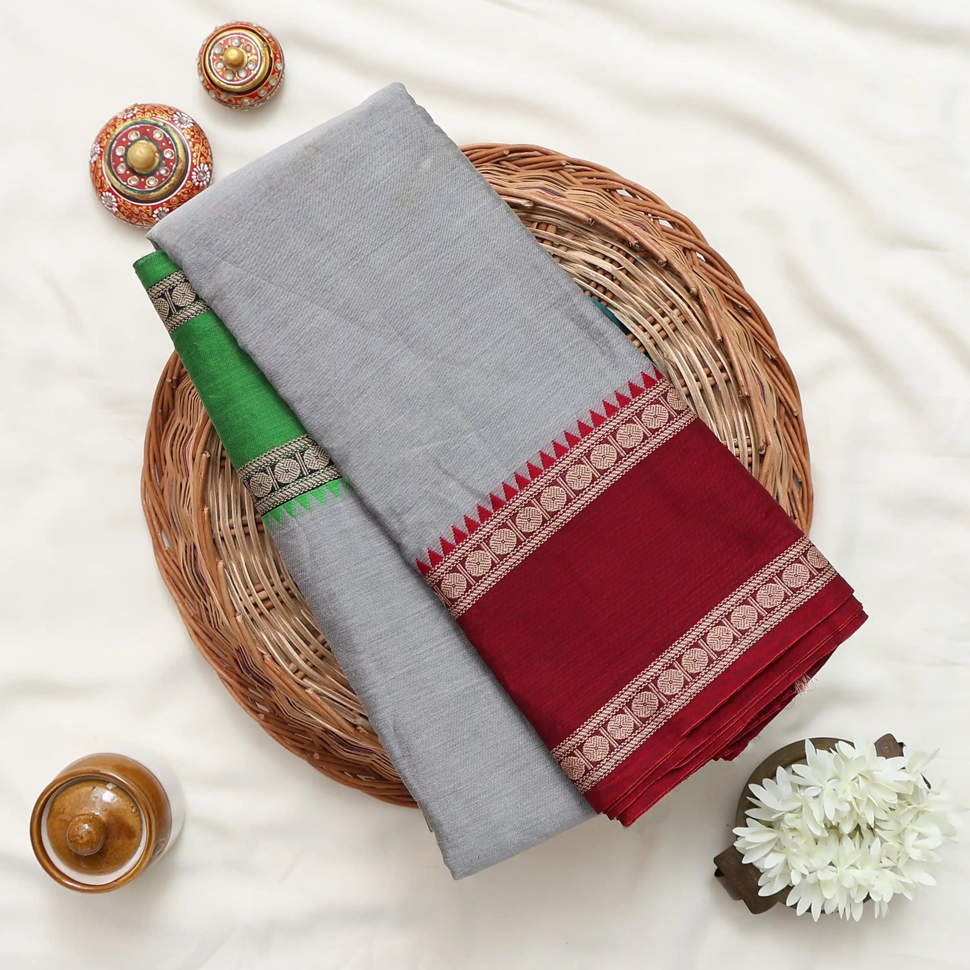 A folded gray fabric garment or textile with a green section and a deep red border featuring intricate gold and white patterns