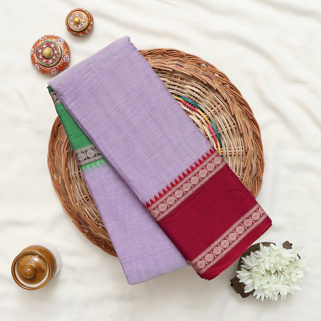 A lavender purple saree with a green and gold checkered border and a deep maroon red pallu