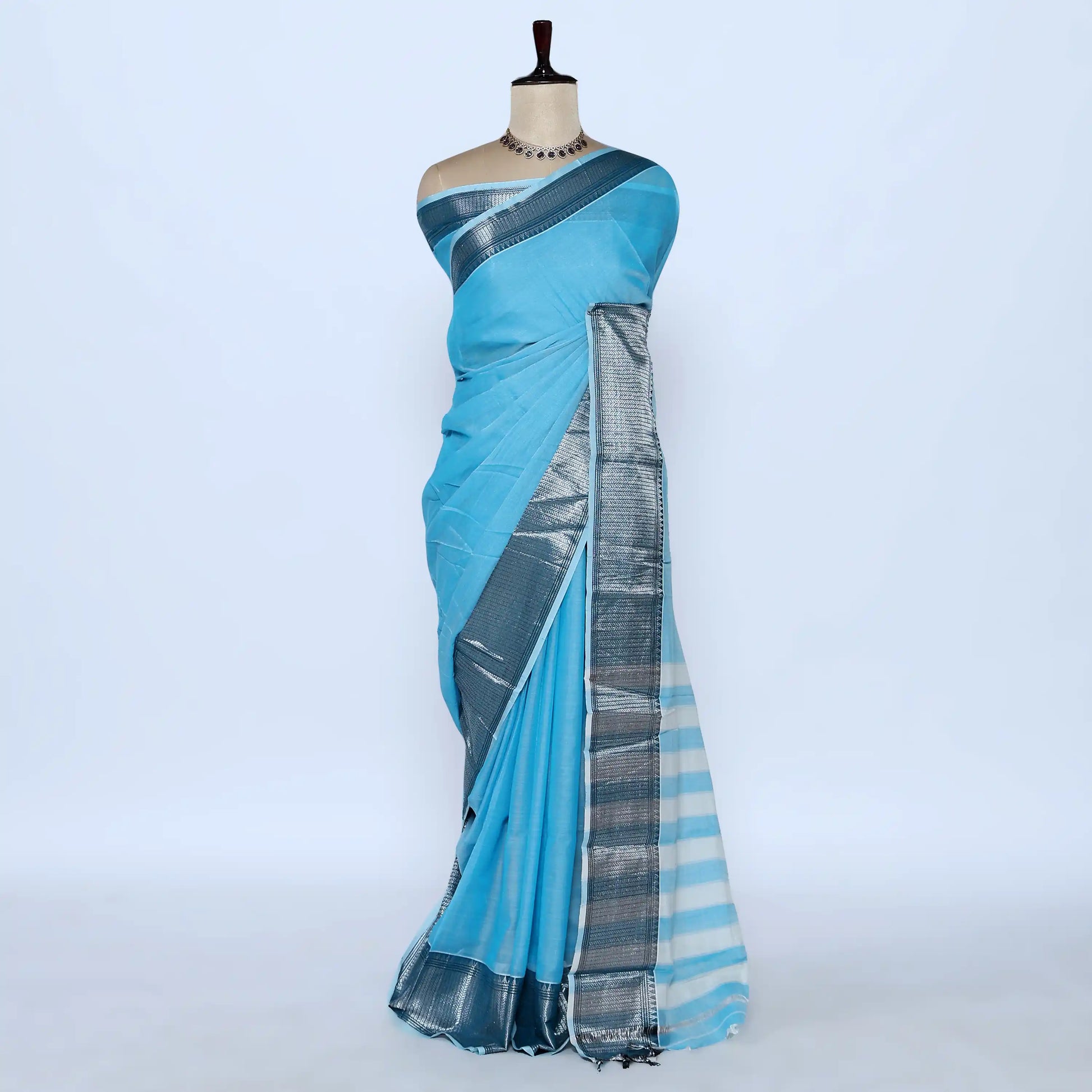 A light blue cotton saree with a metallic silver border and striped pallu