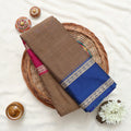 A folded brown and blue saree with a pink border and metallic silver patterned zari