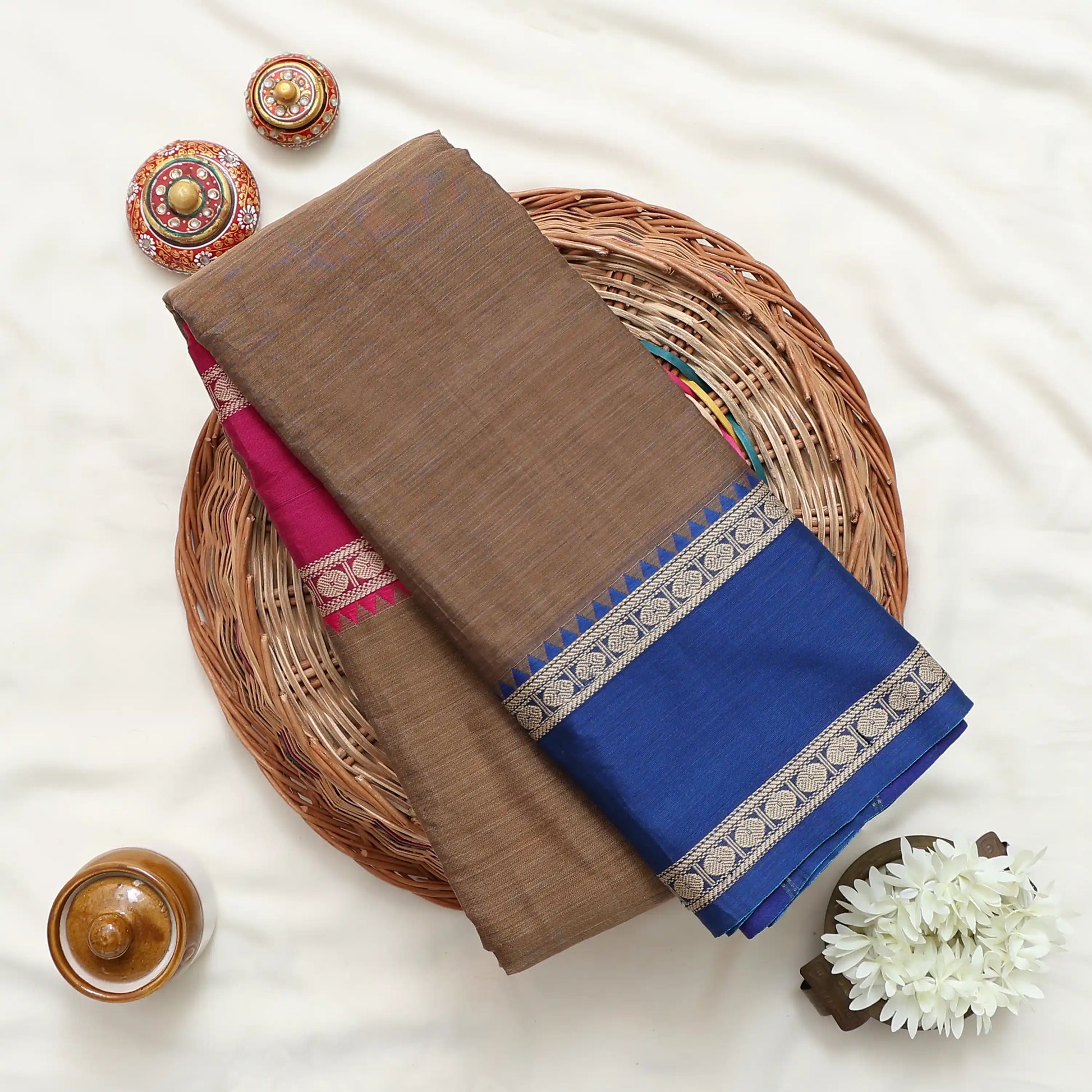 A folded brown and blue saree with a pink border and metallic silver patterned zari