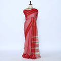 Red and pink saree with gold and green striped border folded on a woven basket display
