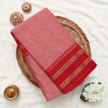 Red and pink saree with gold and green striped border folded on a woven basket display