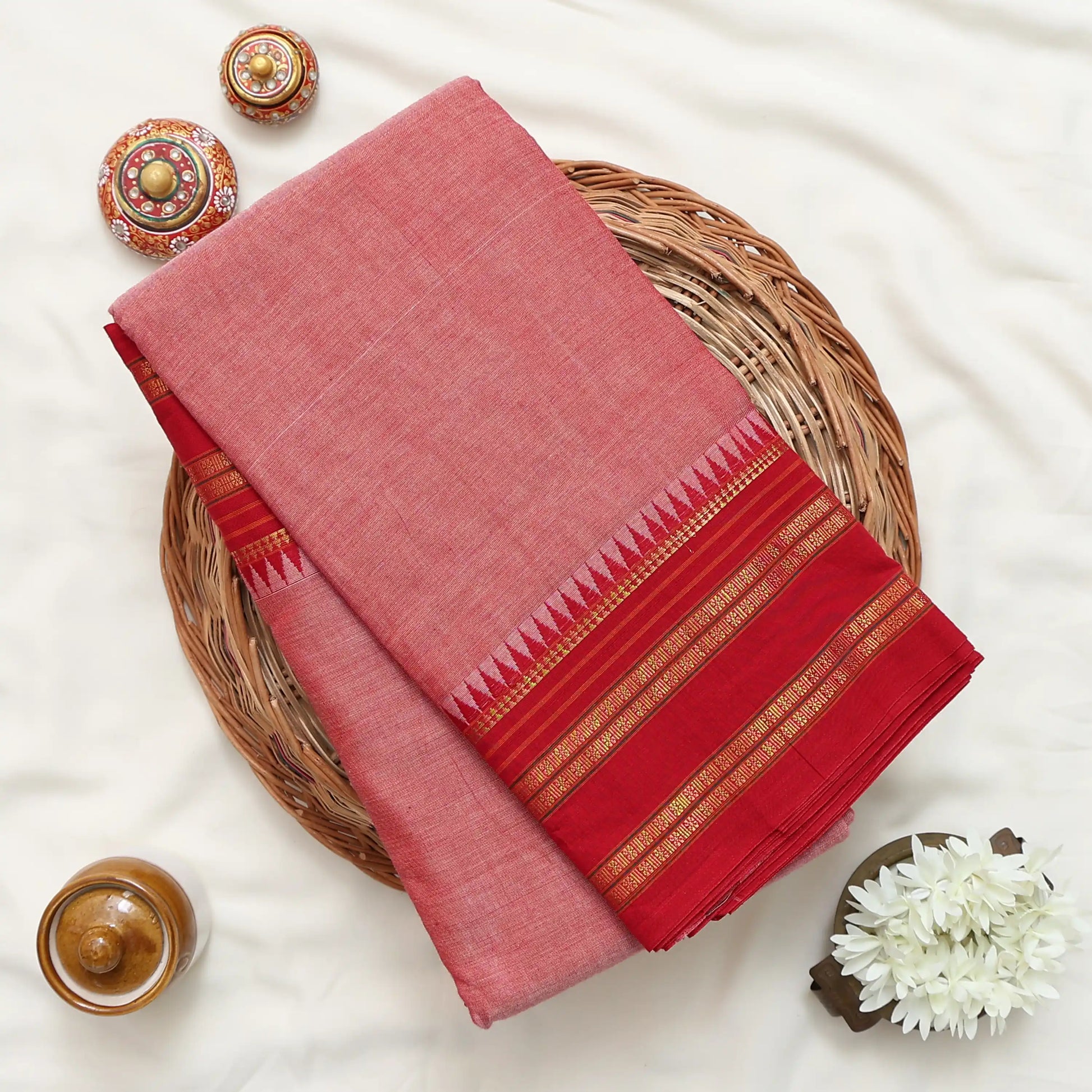 Red and pink saree with gold and green striped border folded on a woven basket display
