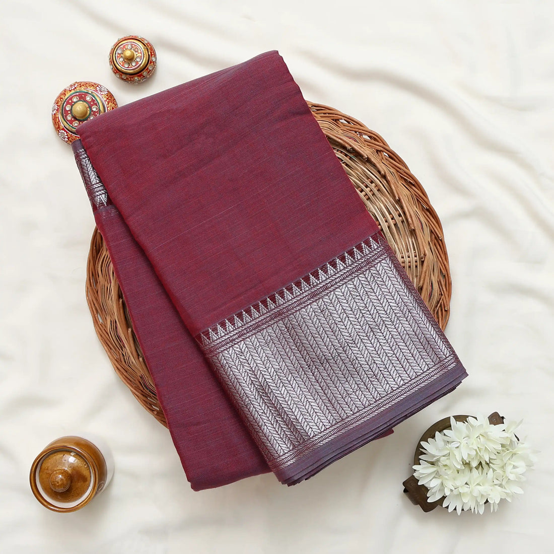 A deep red saree with a metallic silver and gold striped border