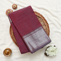 A folded maroon silk saree with a detailed silver and white zari border