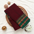 Folded dark maroon and green saree featuring ornate striped border 