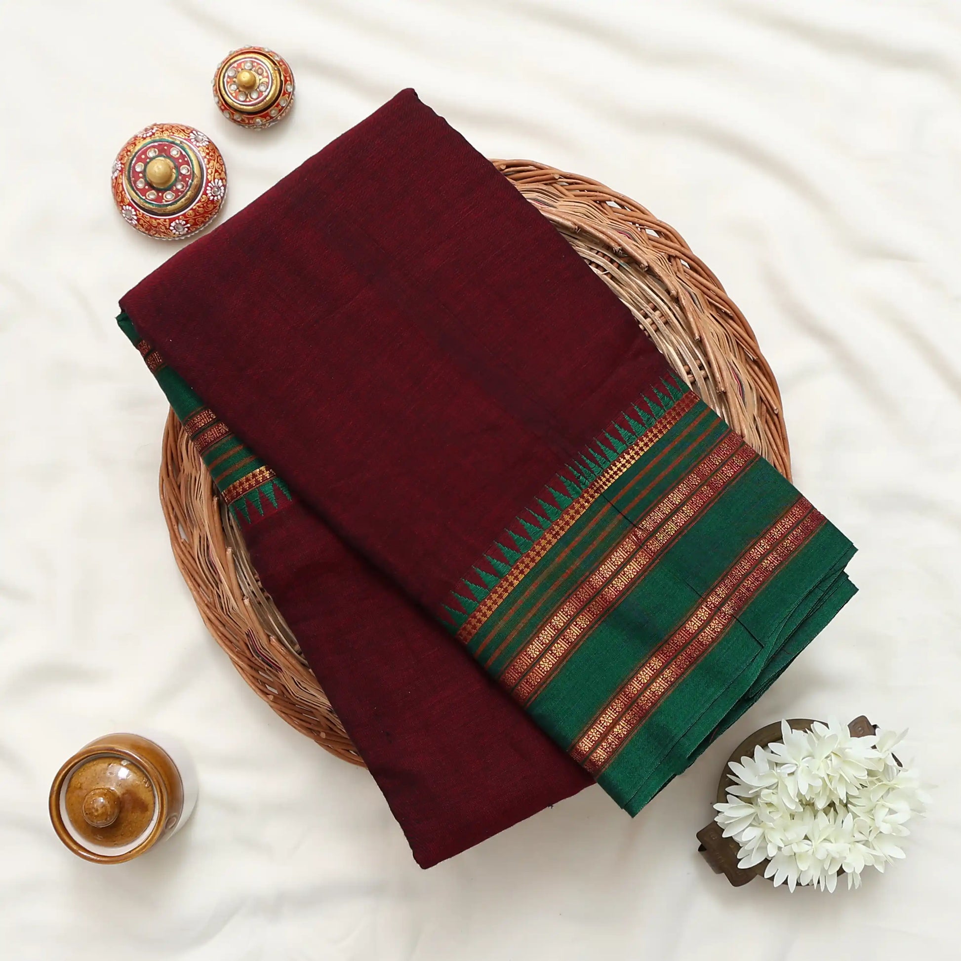 Folded dark maroon and green saree featuring ornate striped border 