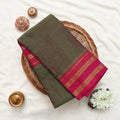 A folded dark olive green saree with a vibrant magenta pink border and gold zari stripes