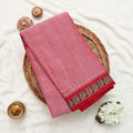 A folded pink cotton saree with a red and gold patterned border