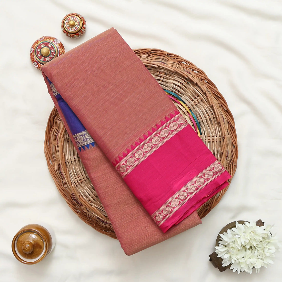 A pink and rust-colored saree with a royal blue border and gold zari stripes