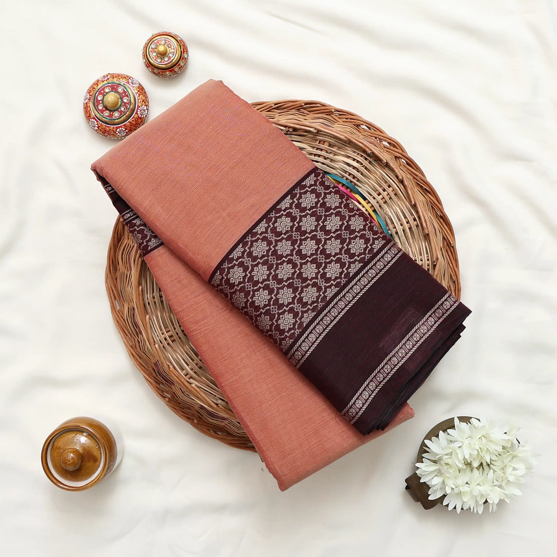 A peach-colored saree with dark brown borders and a patterned pallu