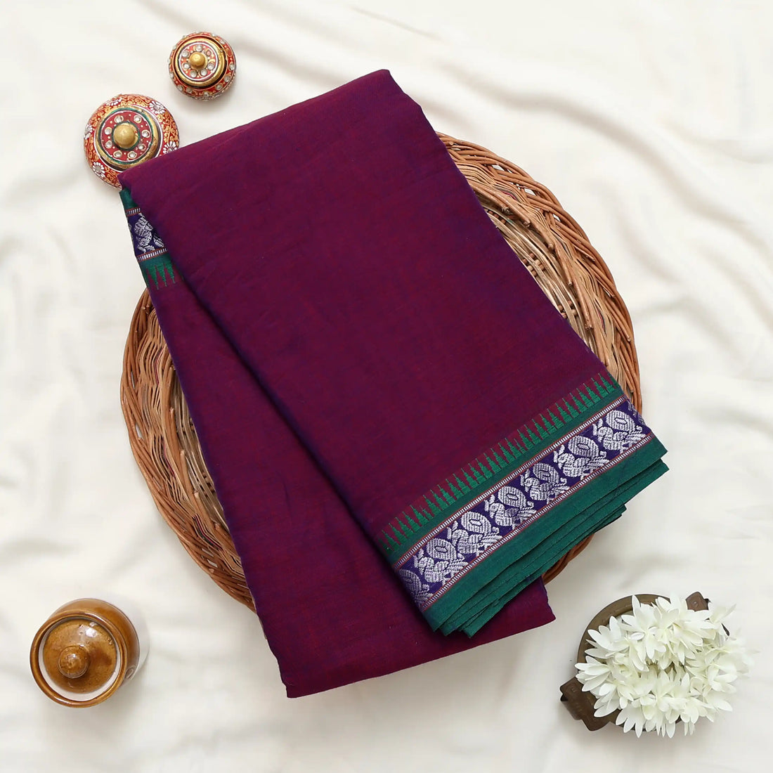 A deep purple saree with green and silver patterned borders