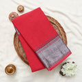 A folded red saree with a silver and red patterned border