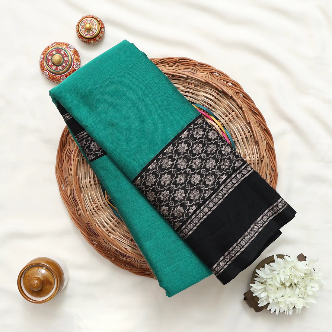 A green and black saree features a solid green body with black borders and a patterned pallu.