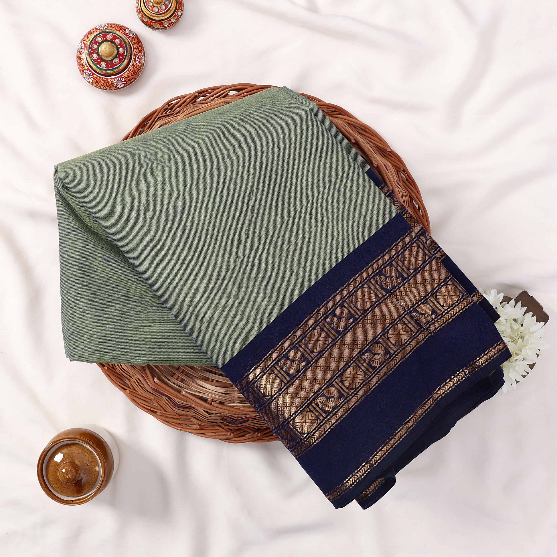 Kanchi Cotton Saree With Solid Olive Green Body And Navy Blue Zari Border Neatly Folded In Basket Top View
