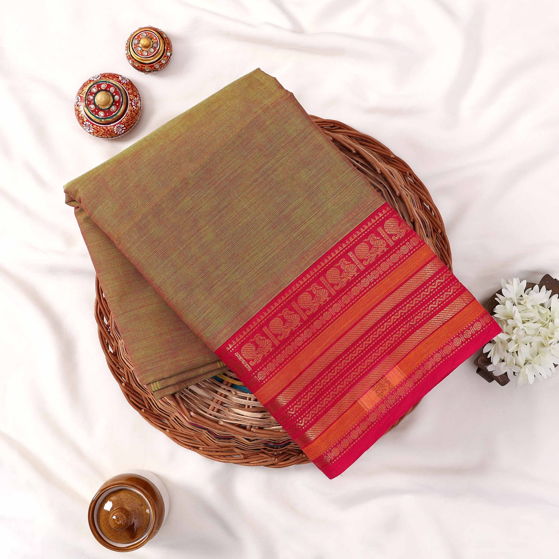 Kanchi Cotton Saree With Olive Green Body And Bright Pink Zari Border Folded Flat Lay View With Decorative Accents
