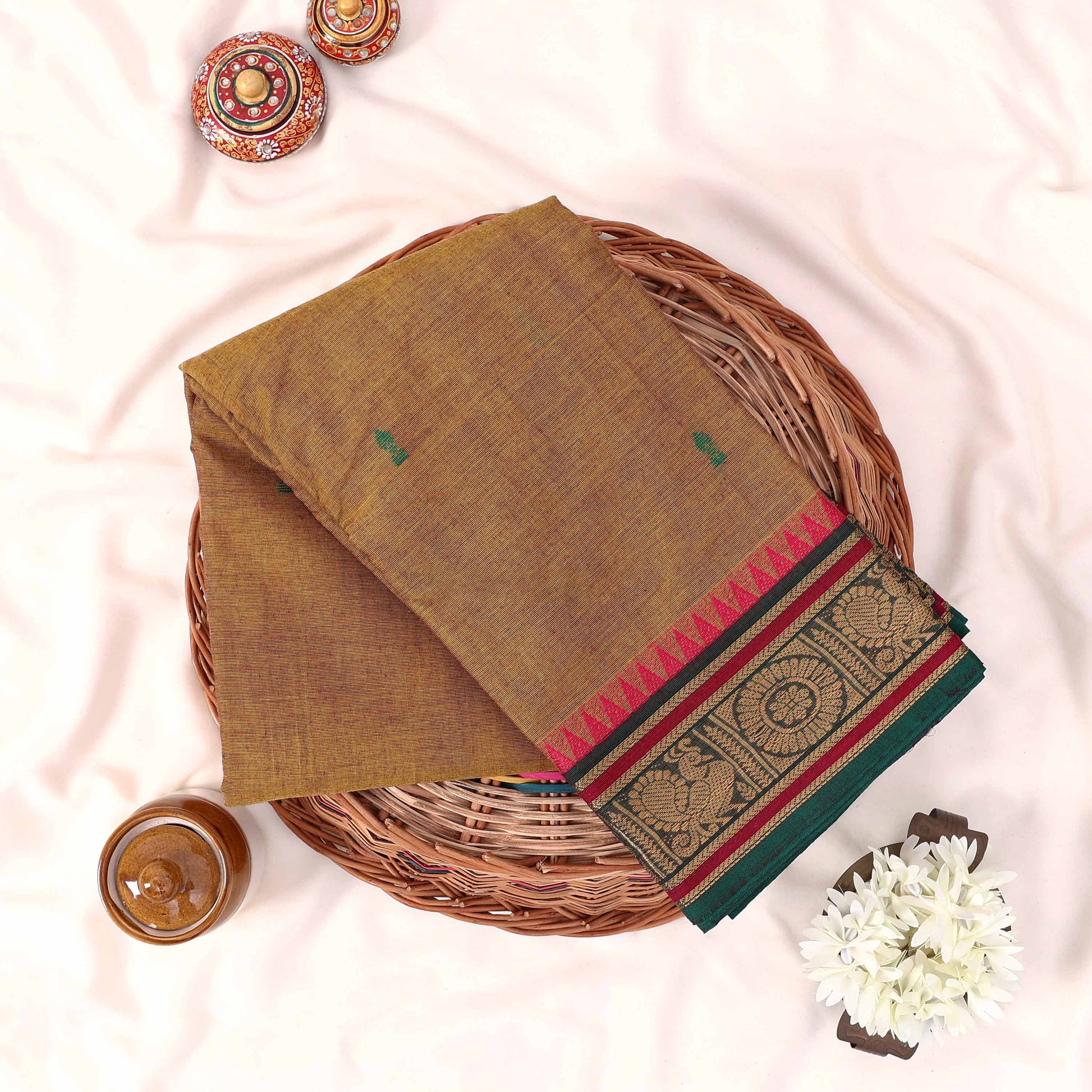 Kanchi Cotton Saree With Traditional Zari Border In Olive Green Neatly Folded On A Wicker Tray Top View
