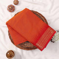Kanchi Cotton Saree With Gold Zari Border In Vibrant Orange And Red Tones, Folded Flat Lay View With Decorative Accents
