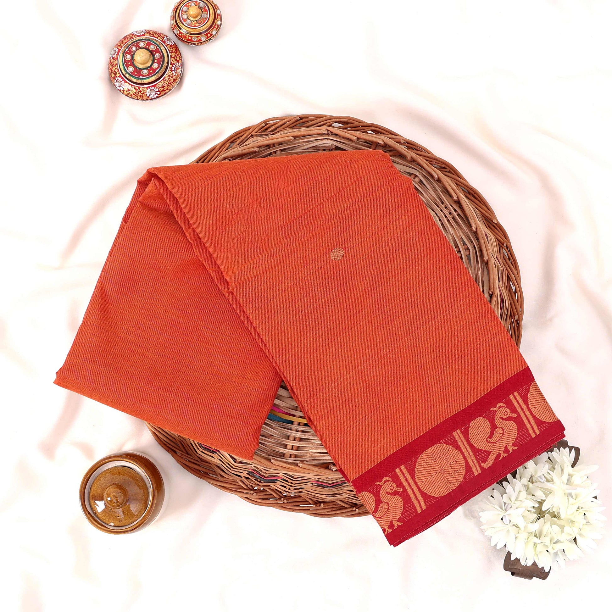 Kanchi Cotton Saree With Peacock Motif Border In Orange Color Folded Flat Lay View With Decorative Accents
