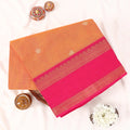 Chettinad cotton saree with orange body pink zari border and delicate woven buttas folded front view on display.