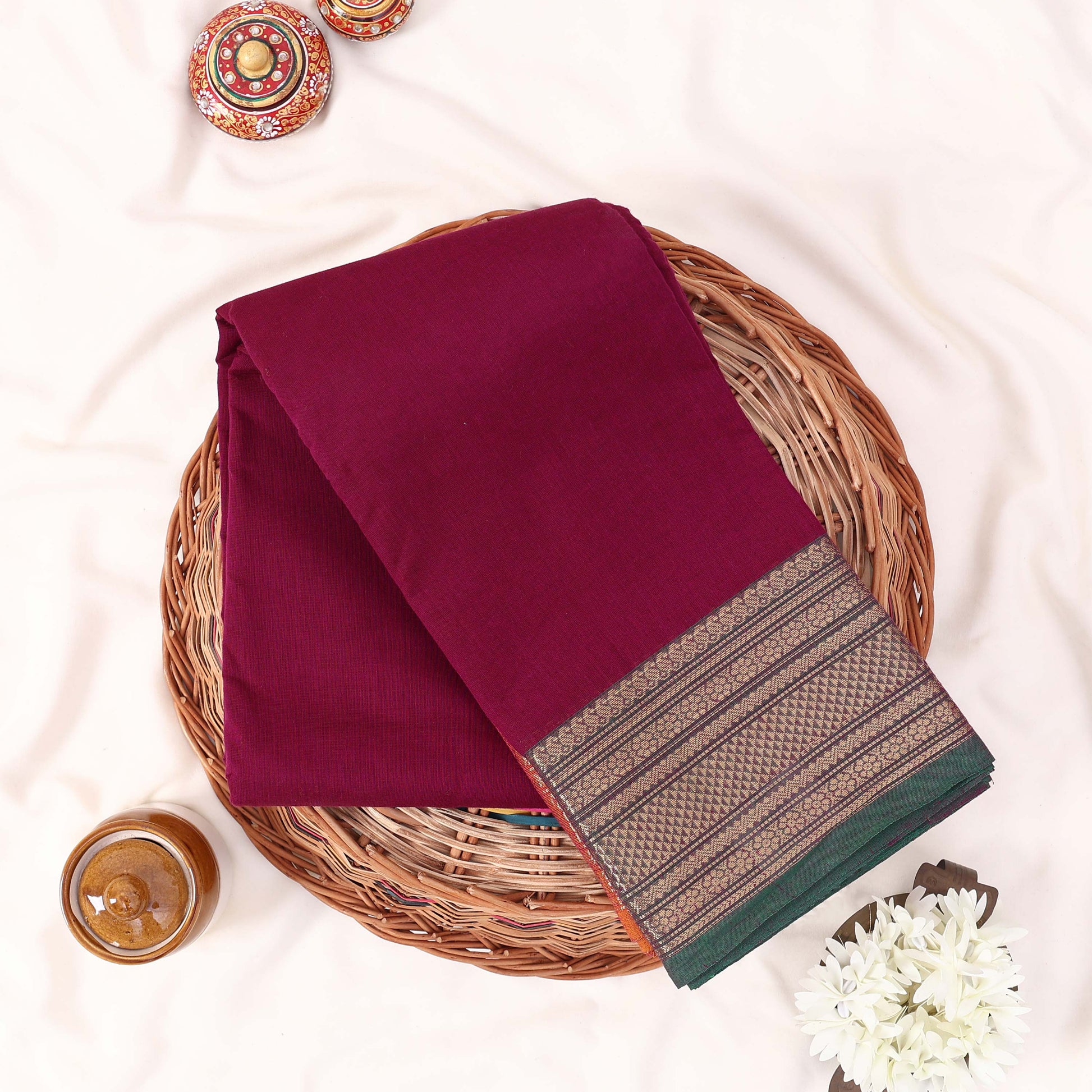 Kanchi Cotton Saree With Zari Woven Border In Deep Purple And Green Folded Flat Lay View With Decorative Accents
