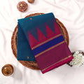 Kanchi Cotton Saree With Teal Body And Magenta Purple Zari Border Folded On Wicker Tray With Floral Décor Top View
