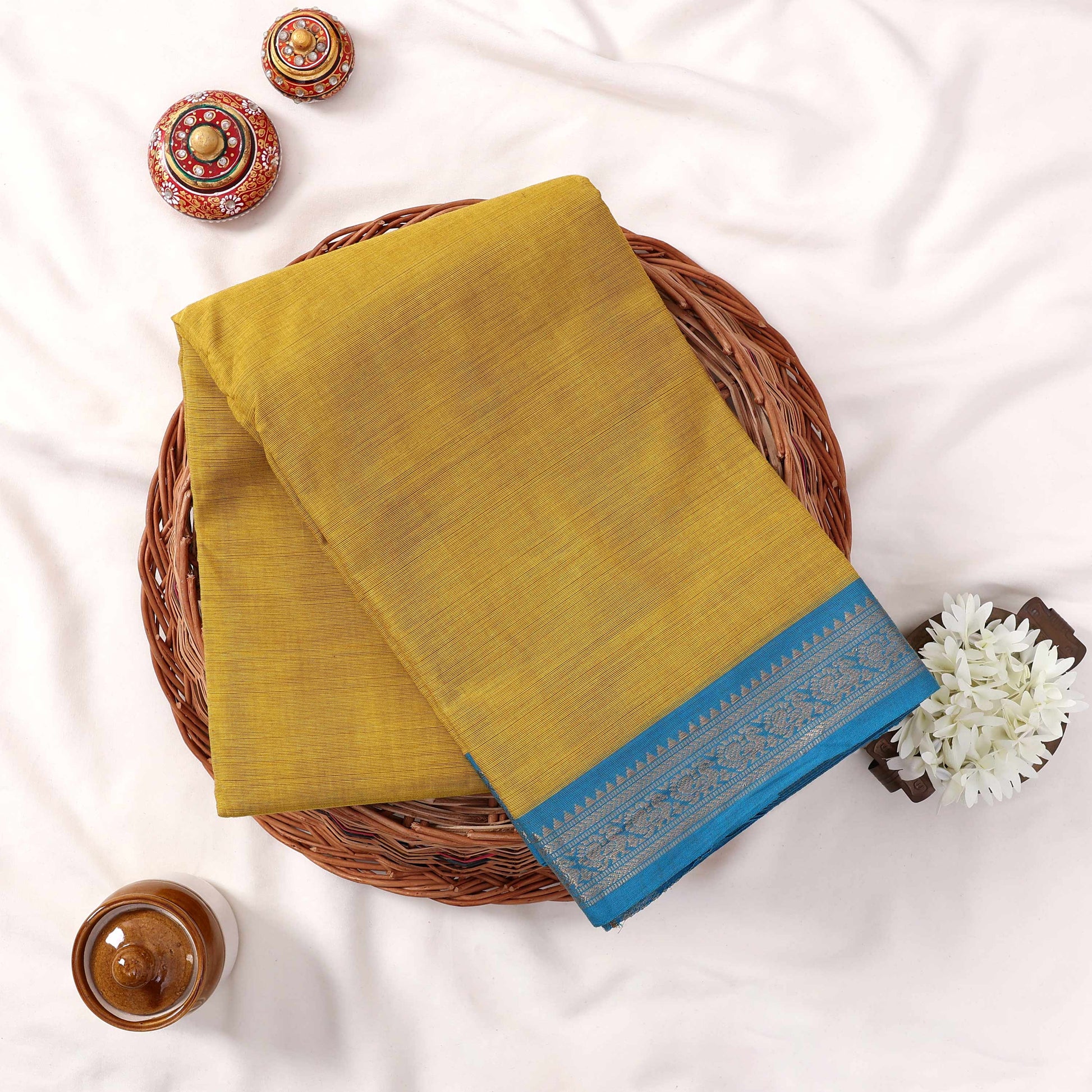 Traditional Kanchi Cotton Saree In Yellow With Contrasting Blue Zari Border Folded Top View Arrangement
