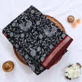 Semi Chanderi saree with white floral and peacock print on black fabric maroon woven border folded top view on wicker tray.