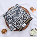 Semi Chanderi saree with floral and peacock print in grey and black folded top view with zari border.