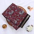 Semi Chanderi saree with white floral and peacock print on red fabric black woven border folded top view on wicker tray.