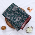 Semi Chanderi saree with white floral and peacock print on teal fabric maroon woven border folded top view on wicker tray.