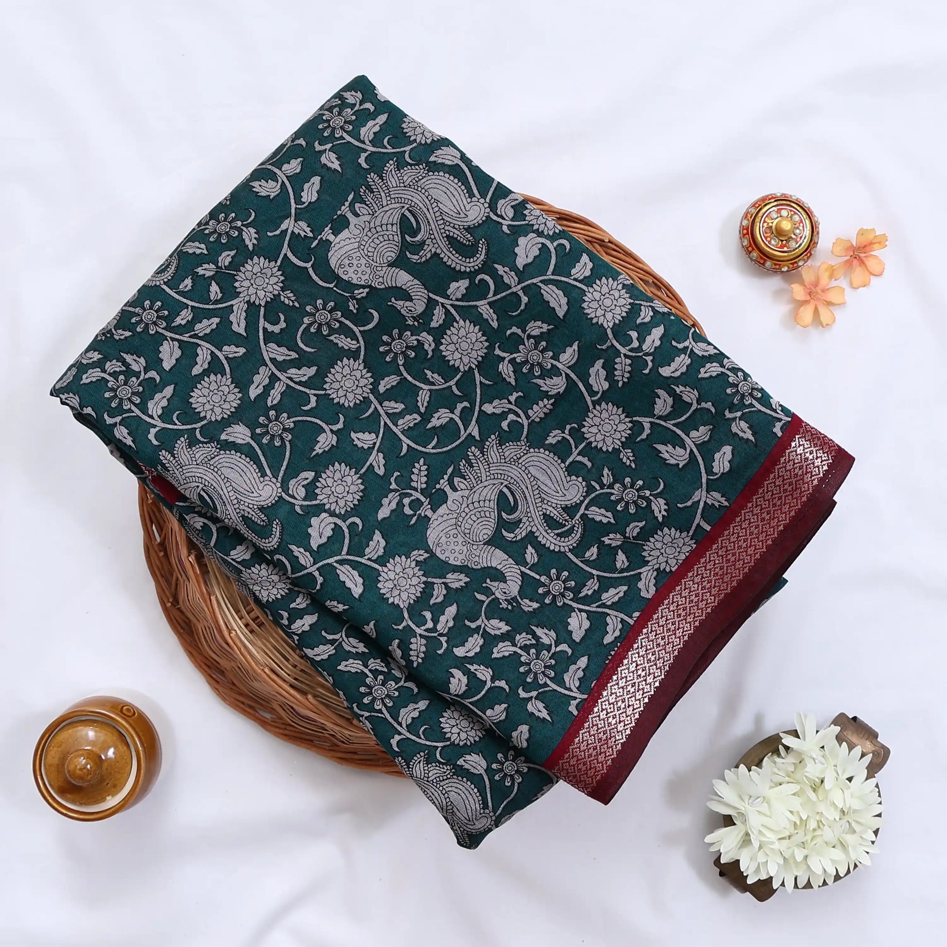 Semi Chanderi saree with white floral and peacock print on teal fabric maroon woven border folded top view on wicker tray.