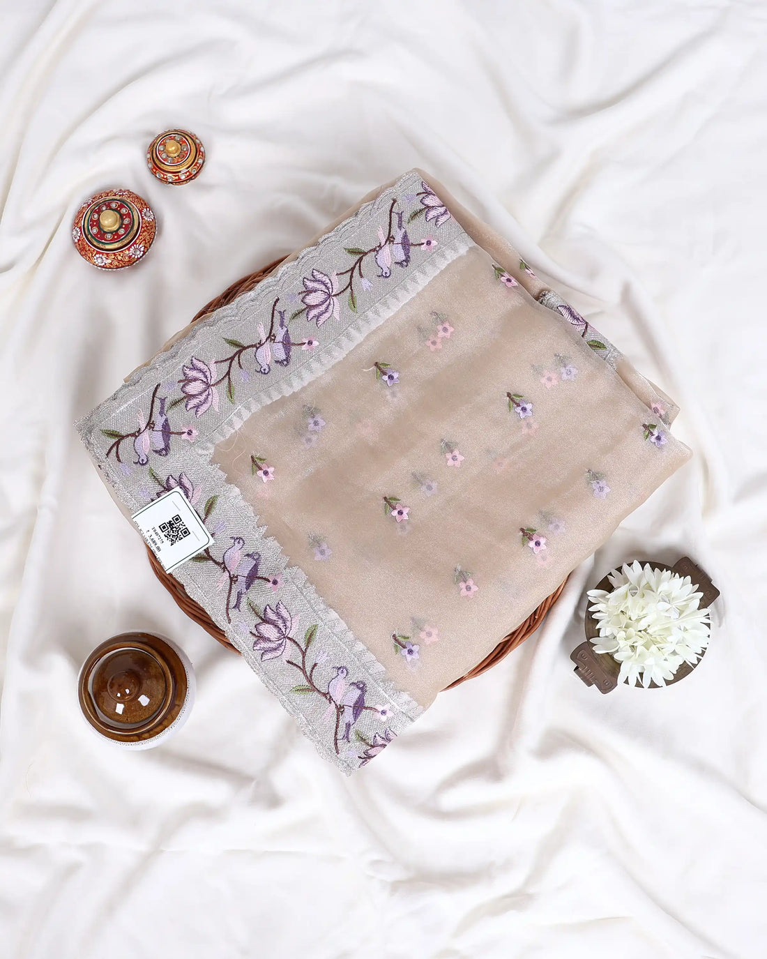A beige saree with purple and green floral embroidery on the border and scattered motifs