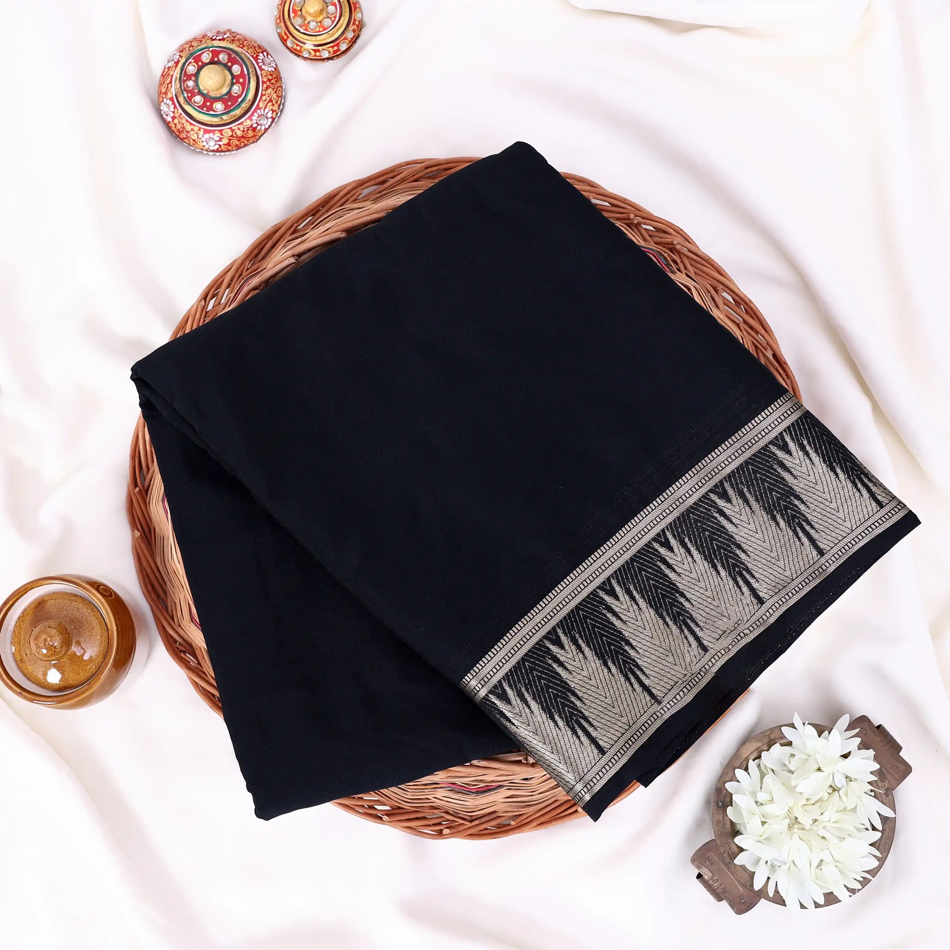 A folded black saree features a decorative border with a gray and black geometric pattern.
