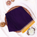 A folded dark lavender mysore silk saree features a wide border with a yellow paisley pattern and metallic silver detailing.