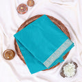 A folded turquoise blue saree  features a decorative light blue and white border pattern along one edge.